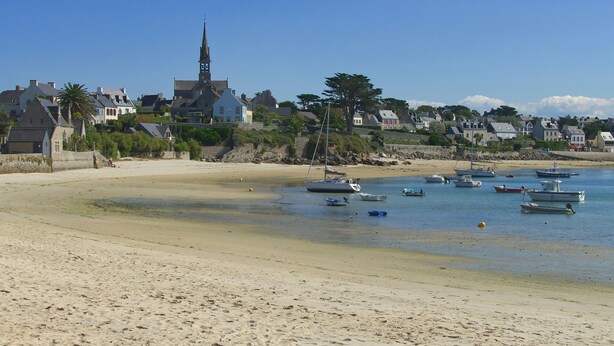 A coastal town with boats on the water, a sandy beach, and houses with a church.
