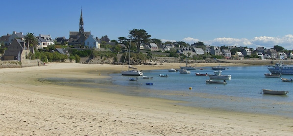 A coastal town with boats on the water, a beach, and houses with a church steeple.