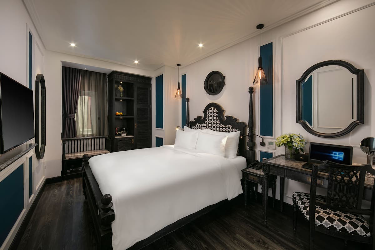 A bedroom with a large bed, a desk with a computer, a chair, and a dresser.