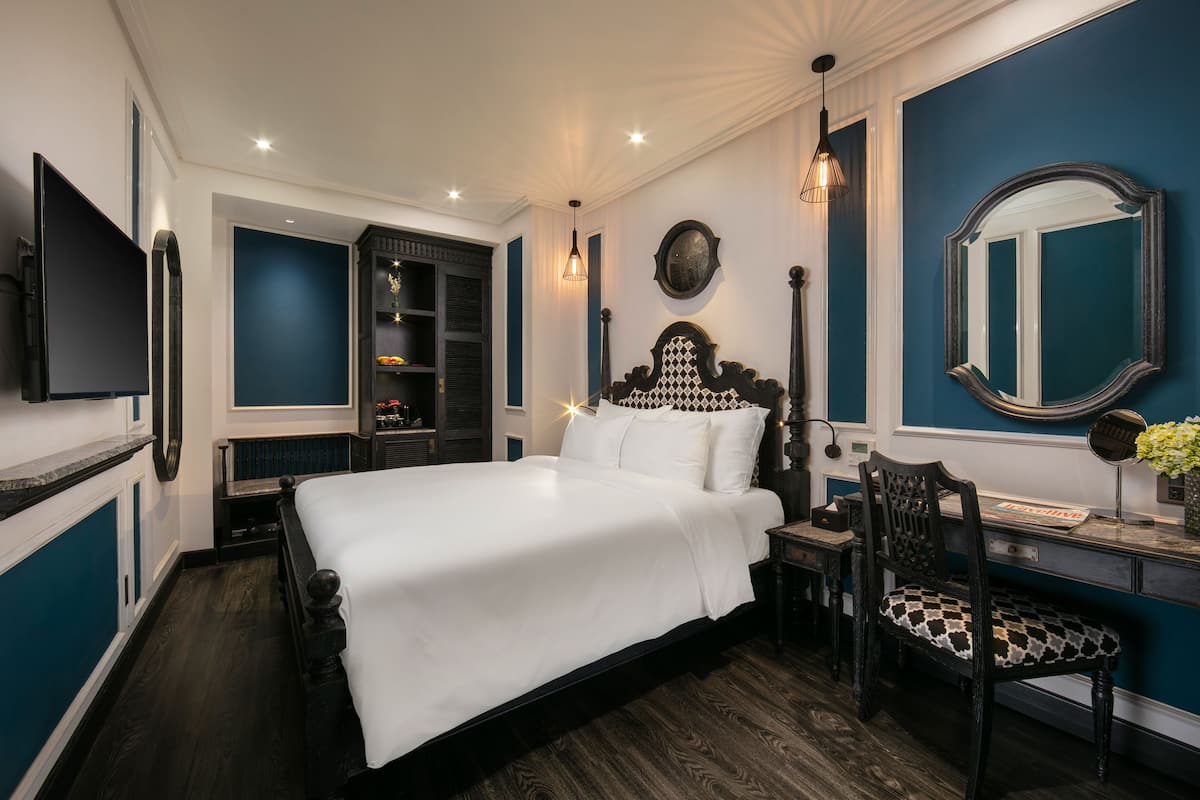 A bedroom with a large bed, a desk, a chair, a TV, and a wardrobe.