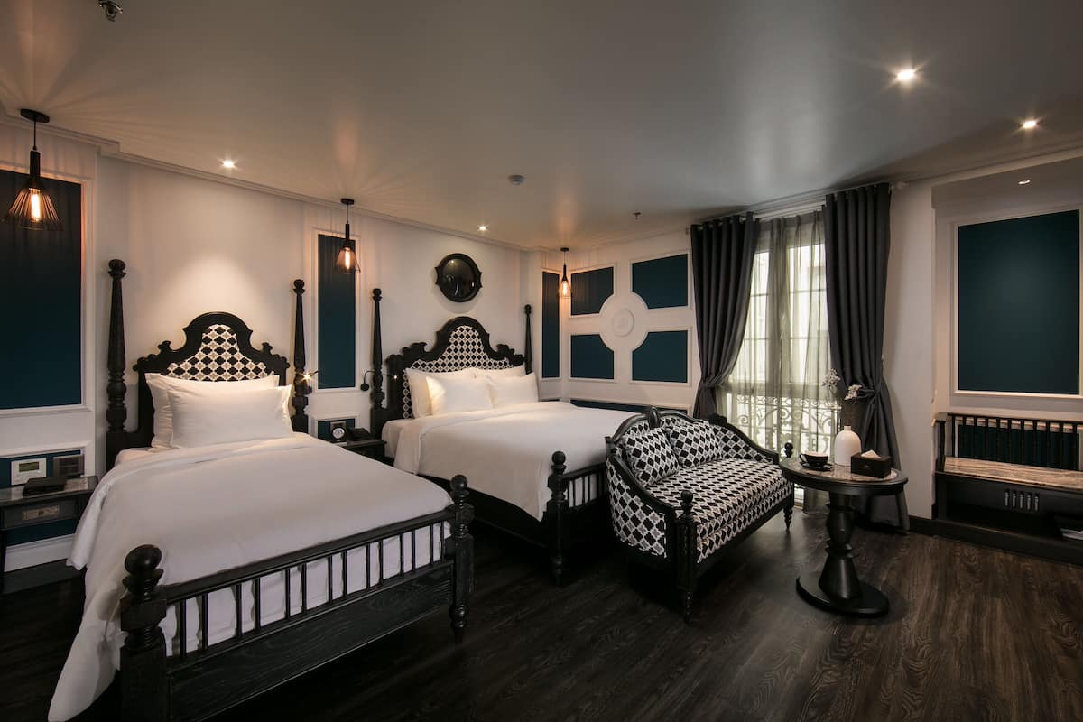 A hotel room with two beds, a sofa, a table, and a window with curtains.