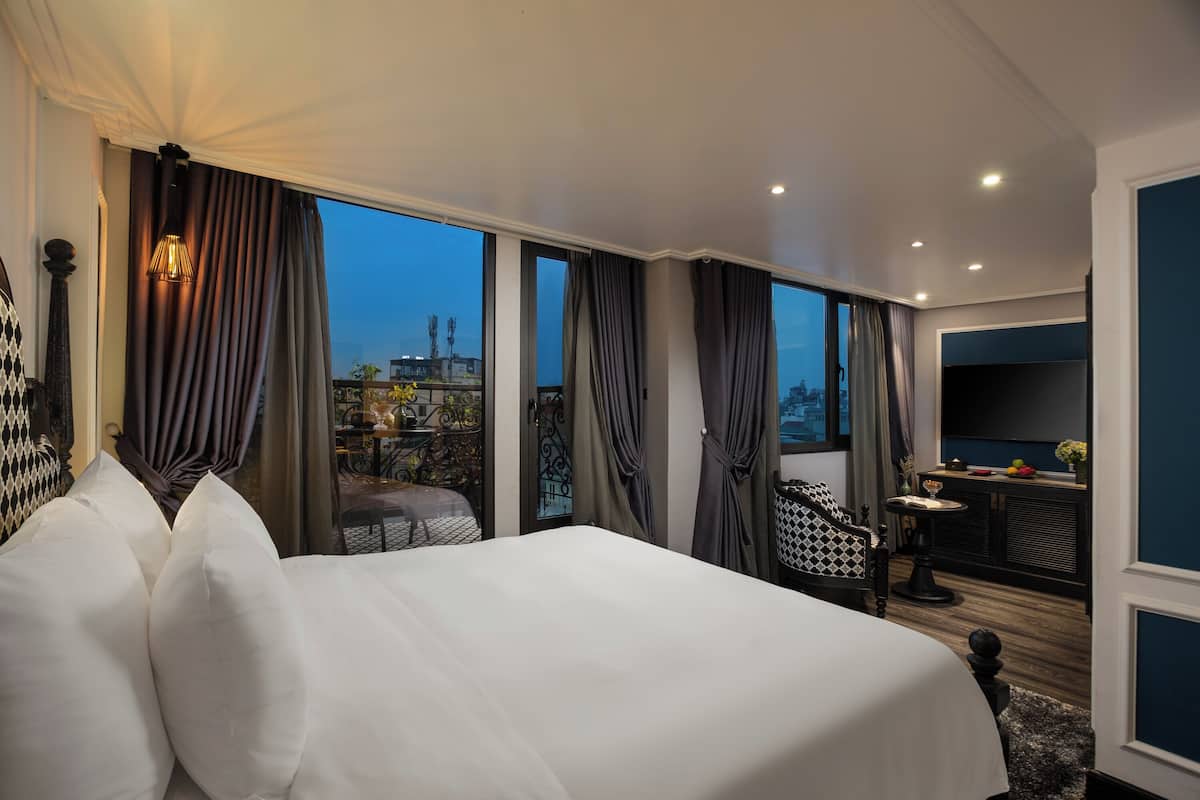 A hotel room with a large bed, a desk, and a view of the cityscape.