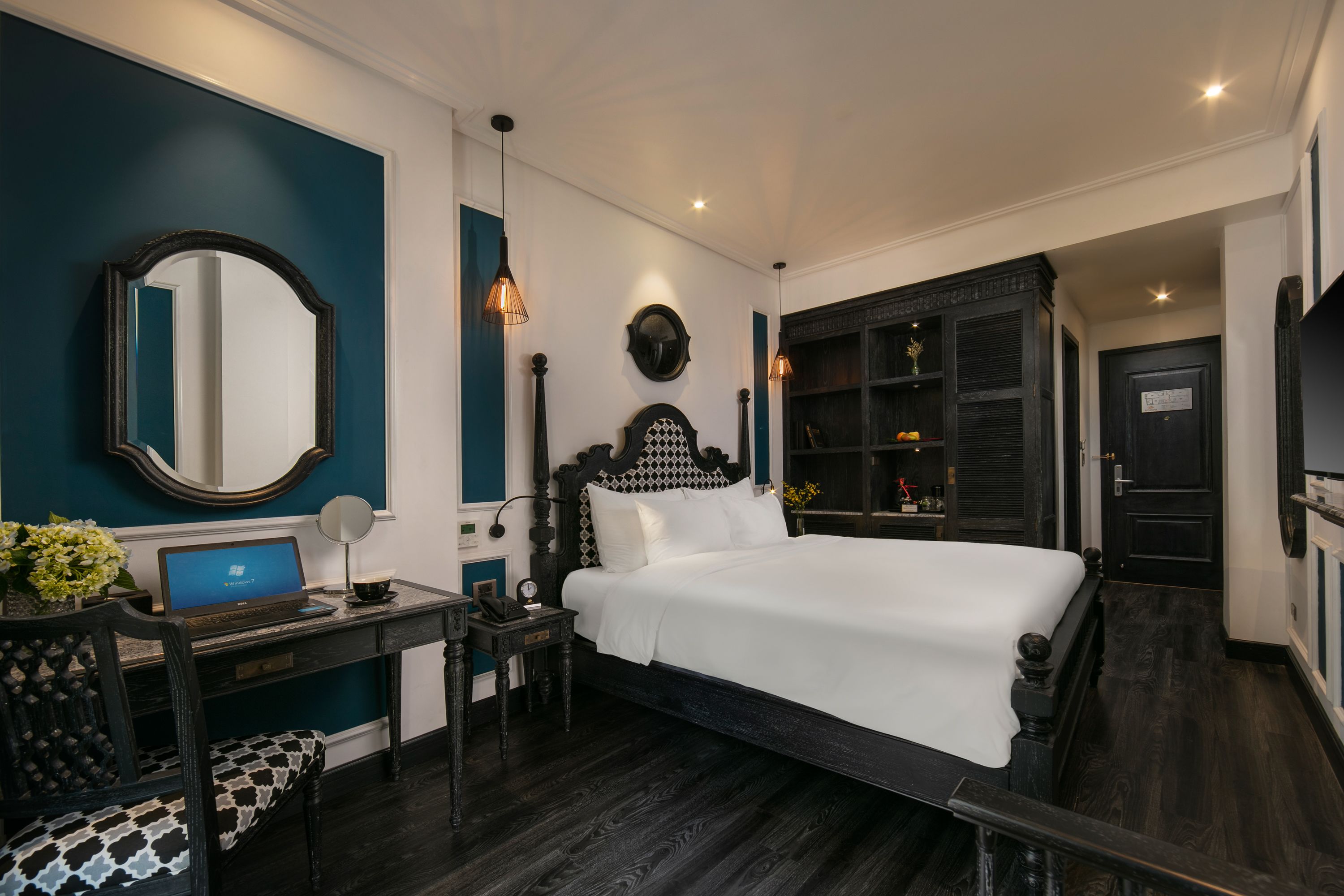 A bedroom with a large bed, a desk with a laptop, a chair, and a dresser.