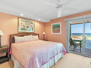 Une chambre dotée d’un grand lit, d’un ventilateur de plafond et offrant une vue sur la plage grâce à une porte-fenêtre coulissante.