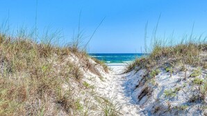 Een zandpad dat naar een strand leidt, met helderblauw water en een heldere lucht.