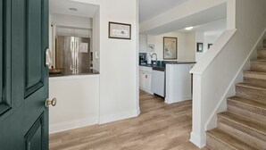 A modern kitchen with white cabinets, stainless steel appliances, and a wooden staircase leading to another level.