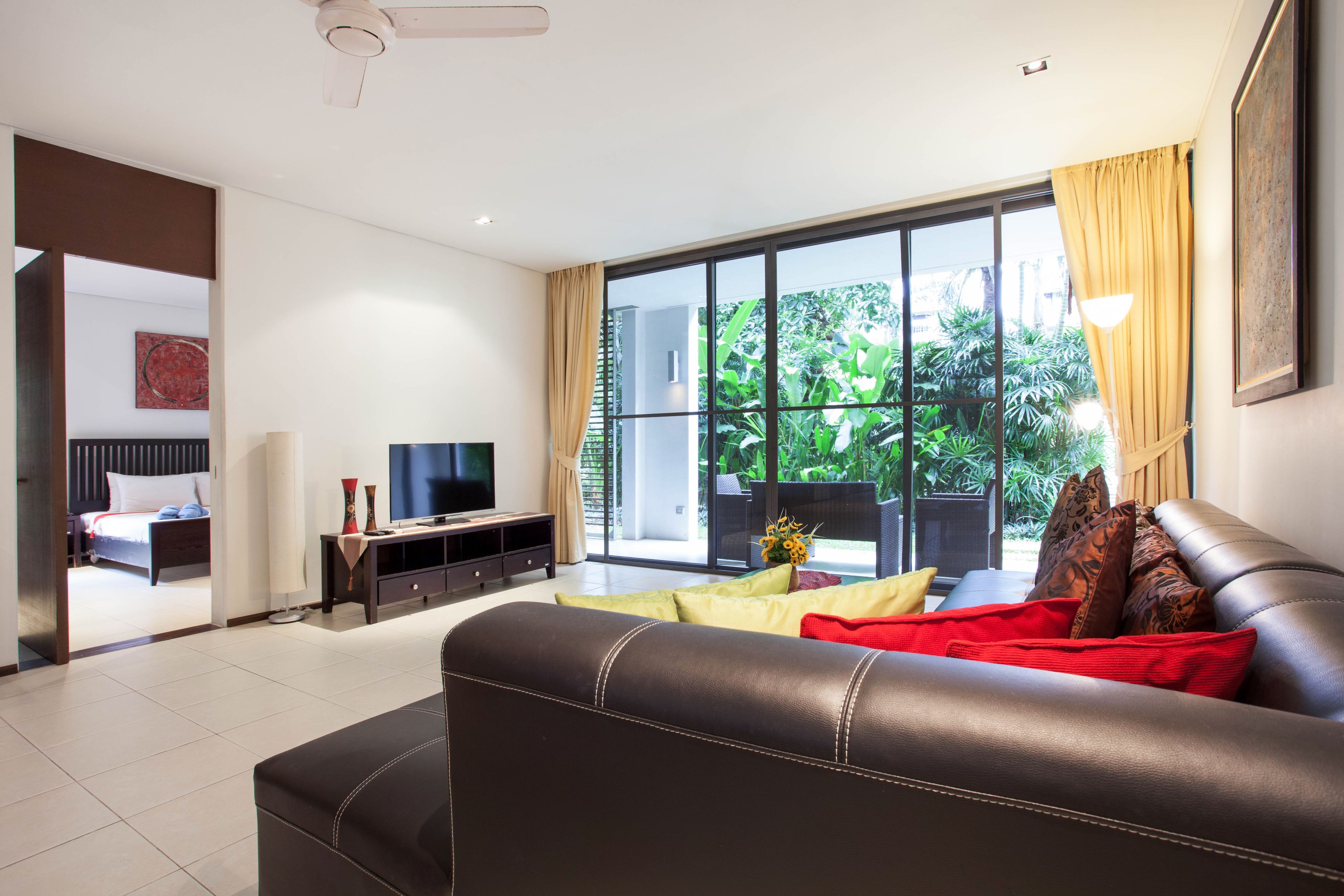 A modern living room with a leather sofa, a flat-screen TV, and a large window with curtains.