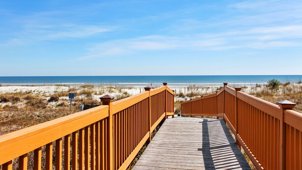 A wooden boardwalk leading to a beach with a clear view of the ocean and sandy dunes.
