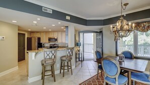 A modern kitchen with a central island, bar stools, and a dining area with a chandelier.