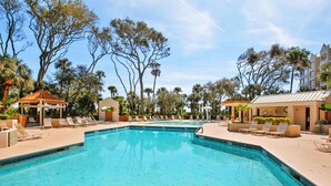 A swimming pool with lounge chairs and a gazebo, surrounded by palm trees and buildings.