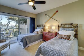 A bedroom with two beds, a ceiling fan, a nightstand with lamps, and a view of the outdoors. - 2316 Windsor II - Beautiful 2 Bedroom Villa with beautiful views! (Hilton Head Island)