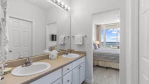 Une salle de bain avec deux lavabos, un grand miroir et une vue sur un balcon où se trouve un lit.