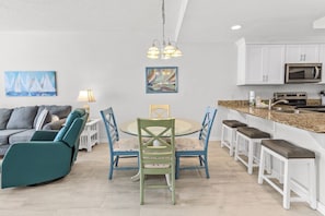 A modern kitchen with white cabinets, a microwave, and a granite countertop. There is a dining area with a round table and blue chairs.