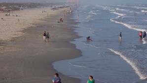 A beach with people walking and swimming.