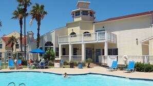 A hotel with a swimming pool, a balcony, and palm trees.