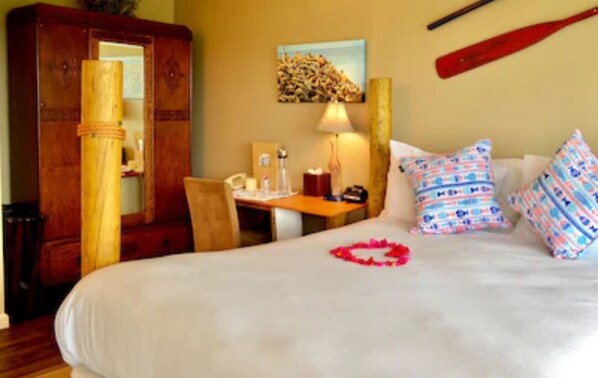 A hotel room with a bed, a desk, a chair, a wooden wardrobe, a lamp, and a baseball bat on the wall.