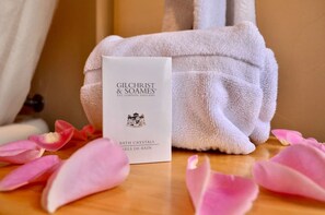 A luxurious box from Gilchrist & Soames, Est. London, England, sits on a surface surrounded by delicate flower petals and a nearby towel.