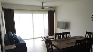 Ein Wohnzimmer mit einem dunkelblauen Sofa, einem Esstisch mit Stühlen, einem Flachbildfernseher und einem Deckenventilator.
