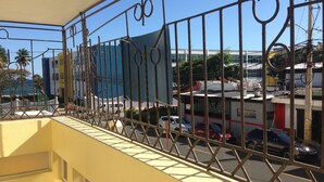 Een balkon met een metalen hekwerk, met uitzicht op een straat met geparkeerde auto's en gebouwen.