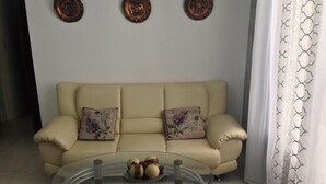 Een woonkamer met een beige bank, twee decoratieve kussens, een glazen salontafel met decoratieve objecten, en drie wandplaten.
