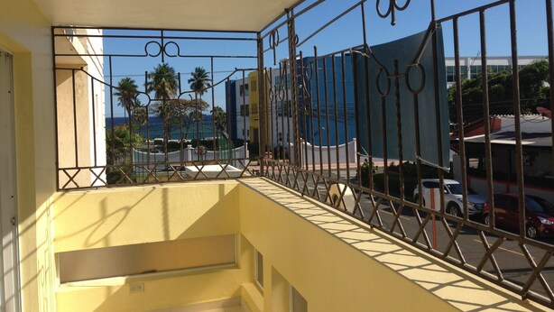 Een balkon met metalen hekwerk, uitzicht op palmbomen en een gebouw op de achtergrond.