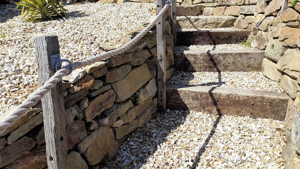 A stone staircase with wooden railings, surrounded by pebbles and a small plant. - 3 bedroom accommodation in Mount Hawke, near St Agnes (Mount Hawke, near St Agnes)