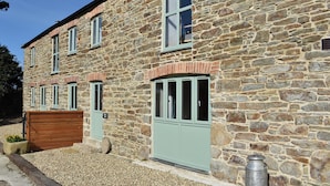 A stone building with multiple windows and doors, a wooden bench, and a metal container. - 3 bedroom accommodation in Mount Hawke, near St Agnes (Mount Hawke, near St Agnes)