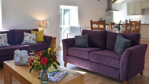A living room with two purple sofas, a coffee table with a vase of flowers, and a view into the kitchen. - 3 bedroom accommodation in Mount Hawke, near St Agnes (Mount Hawke, near St Agnes)