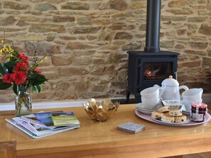 A wooden table with magazines, a vase of flowers, a decorative bowl, a tray with biscuits and jam, and a white kettle.