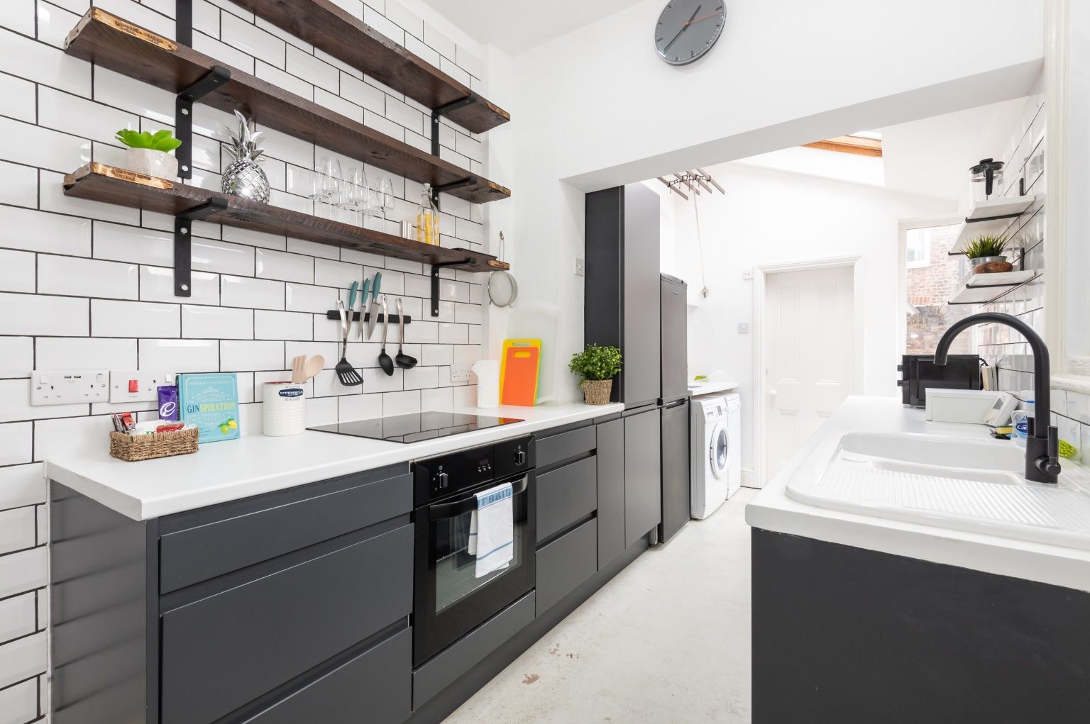 A modern kitchen with white subway tiles, black cabinetry, and wooden shelves.