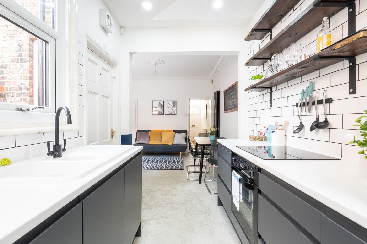 A modern kitchen with white countertops, black cabinets, and a dining area with a sofa and table.