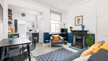 A modern living room with a fireplace, a dining area with a table and chairs, and a kitchen in the background.