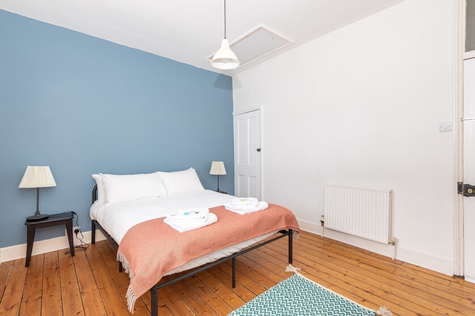 A bedroom with a bed, two bedside lamps, a radiator, and a door.