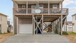 Une maison à deux étages avec un balcon à l’étage supérieur, un garage et une enseigne sur laquelle on peut lire : « Sweet Tea by the Sea ».