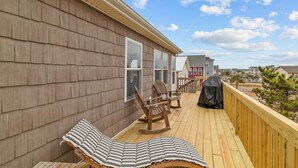 Une terrasse en bois avec des chaises longues et un barbecue.