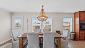 Un coin repas avec une table en bois et six chaises, un lustre et une vue sur le quartier grâce à de grandes fenêtres.