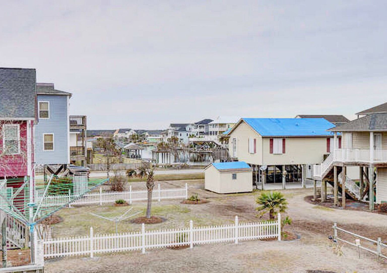 Zona residencial costera con casas, un pequeño patio cercado y un parque infantil.
