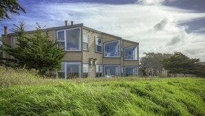 Et moderne hus i to etager med store vinduer og et fladt tag, omgivet af frodigt grønt.