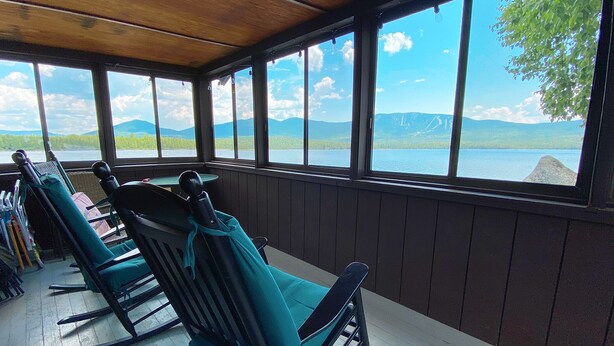 Une terrasse couverte, dotée de fauteuils à bascule, qui offre une vue sur un lac et des montagnes.