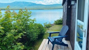 Une terrasse en bois avec une chaise, d’où l’on a vue sur un lac et des montagnes.