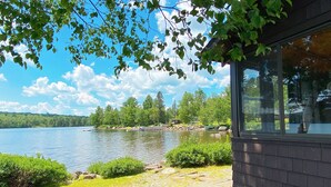 Une propriété au bord du lac, dotée d’un quai, d’une construction en bois avec de grandes fenêtres, et offrant une vue sur le lac et les arbres environnants.