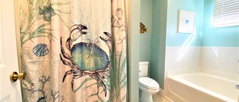 A bathroom with a shower curtain featuring sea creatures, a white bathtub, and a toilet.