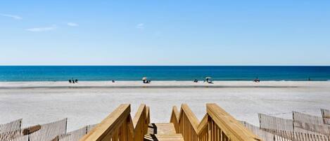 A wooden boardwalk leading to a beach with a clear blue sky.