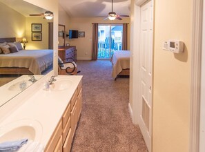 A hotel room with a double sink, two beds, a ceiling fan, and a view of the outside balcony.