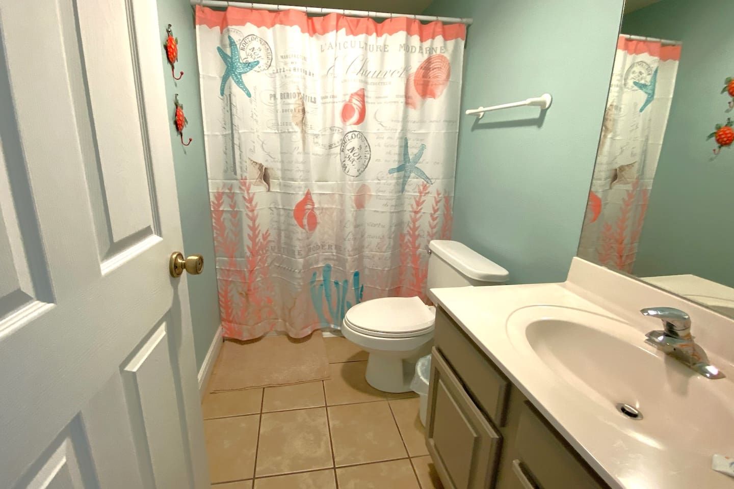 Une salle de bain équipée de toilettes, d’un lavabo et d’un rideau de douche décoré sur le thème de la mer.