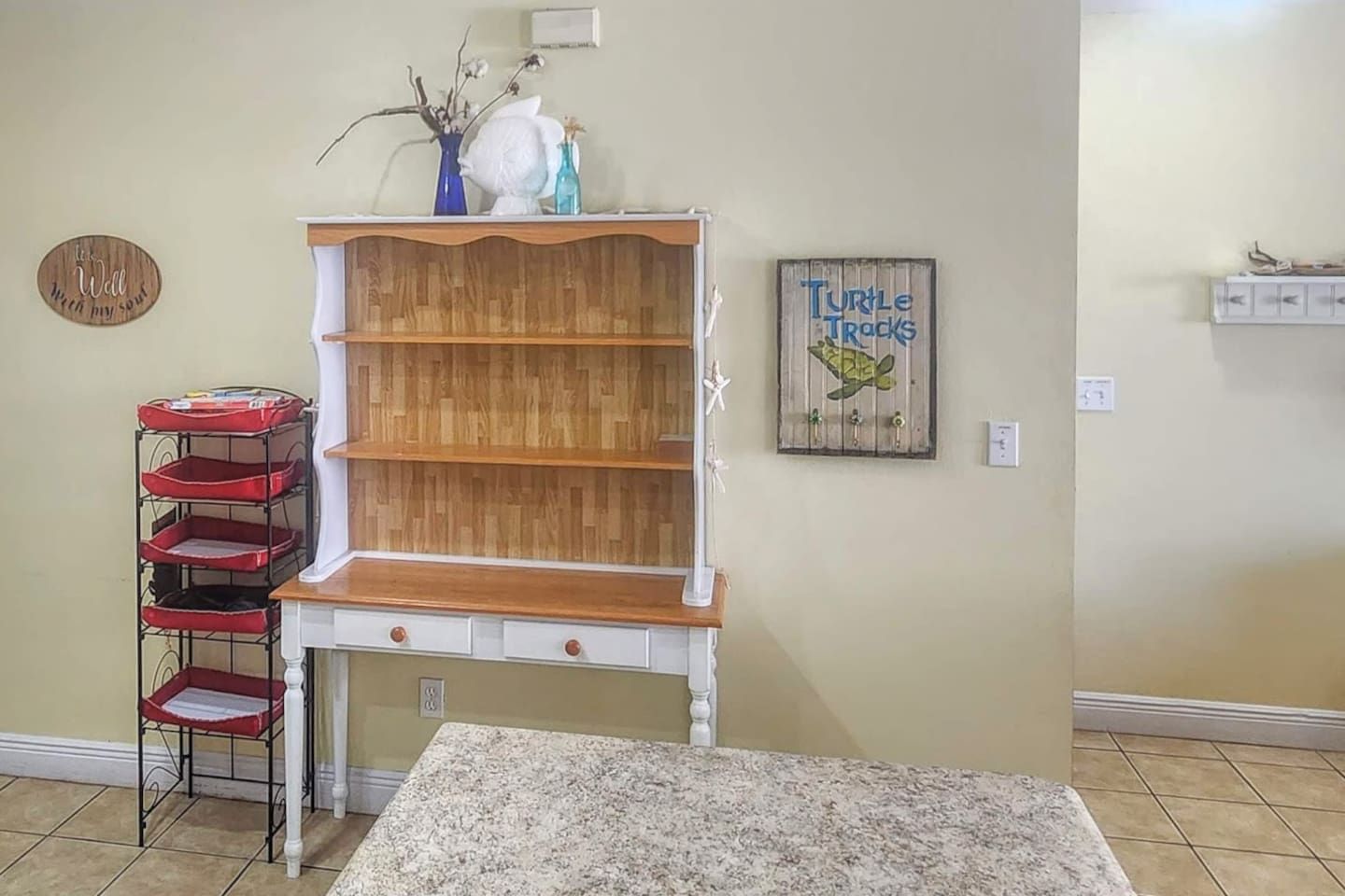 A kitchen with a wooden cabinet, a red and white metal rack, and a 'Turtle Tracks' sign on the wall.