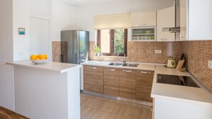 Een moderne keuken met witte kasten, een roestvrijstalen koelkast, een spoelbak en een raam met uitzicht op groen.