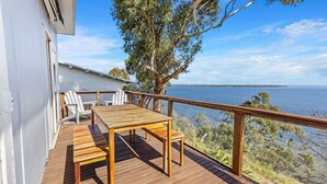 A wooden deck with a table and chairs, overlooking a body of water. - Lakescapes Cottage: Relax & enjoy 180 degrees, uninterrupted water views (Metung)