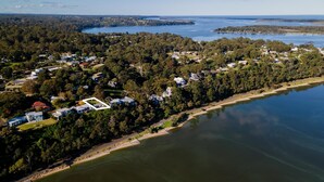 An aerial view of a residential area with houses, dense trees, and a large body of water. - Lakescapes Cottage: Relax & enjoy 180 degrees, uninterrupted water views (Metung)