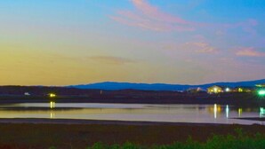 Ein See bei Dämmerung mit entfernten Häusern und ruhiger Wasseroberfläche.